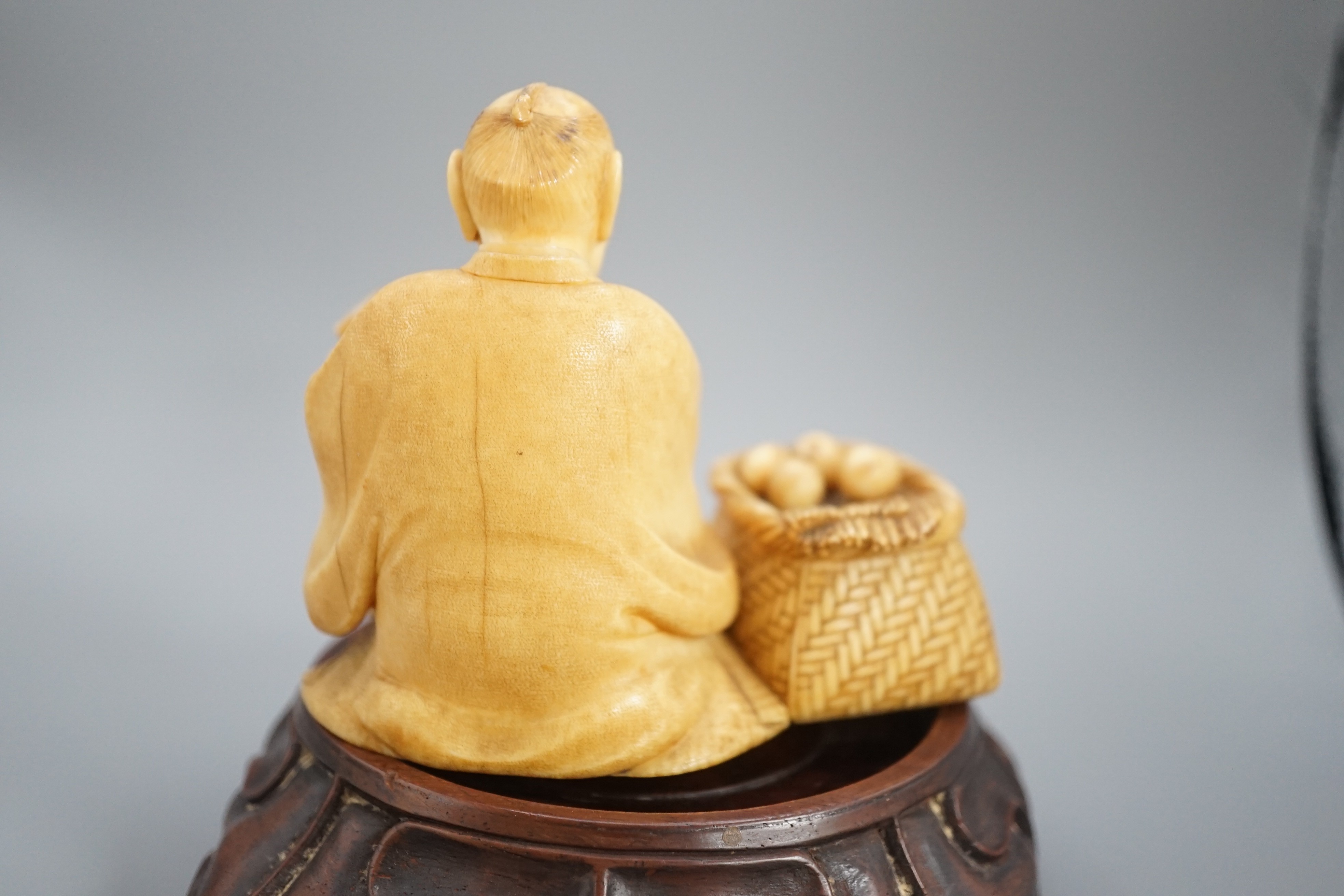 A Japanese ivory okimono of a street vendor kneeling and holding an abacus, Meiji period, 8cm, associated wood stand